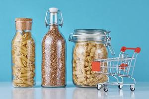 Empty shopping trolley, pasta and buckwheat on a blue background photo