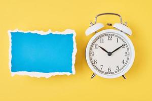 White alarm clock and empty torn paper sheet on a yellow background photo