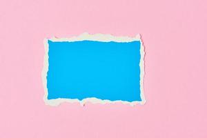 Ripped blue paper torn edge sheet on a pink background. photo