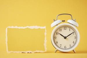 Classic alarm clock with bells and empty torn paper sheet on the yellow background photo