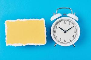 White alarm clock and empty torn paper sheet on a blue background photo