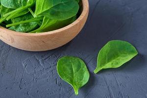 Fresh spinach leaves in wooden bowl on dark background. Organic food photo