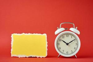 Classic alarm clock with bells and empty torn paper sheet on the red background. photo