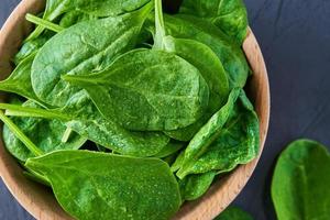 Fresh spinach leaves in wooden bowl on dark background. Organic food photo