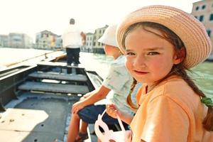 Baby girl hold venetian mask in hands and sit in gondola in Venice,  Italy. photo