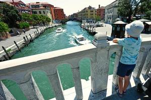 parte posterior del stand de niño en el puente del canal con barcos en venecia, italia. foto