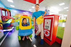 Brother with sister playing at indoor play center playground in toy car gas station. photo