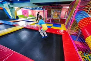 Happy kids playing at indoor play center playground. Boy jumping on trampoline. photo