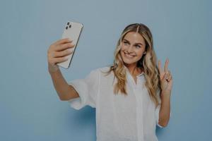 Blonde teenage girl showing peace sign while taking selfie on smartphone photo