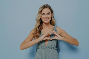 Blonde teenager girl showing heart gesture with her hands photo