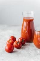 Vertical shot of fresh red tomato juice in glass, red fresh raw tomatoes near on white background. Making ketchup. Organic drink photo