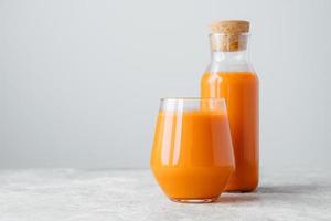 Fresh carrot juice in bottle with cork and glass, isolated over white background with copy space for your information. Healthy drinking concept photo