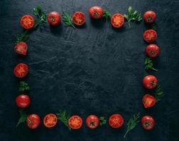 Composition of red tomatoes and green fresh parsley and dill lying on dark background in form of frame. Vegeterian food concept. Free space in middle photo