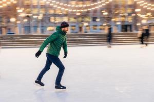 el hombre de mediana edad usa patines de figuras, está en la pista de hielo en el parque de invierno, se divierte con un amigo. el patinador de velocidad del atleta demuestra su talento en la pista de patinaje. deporte de invierno. vacaciones de navidad foto