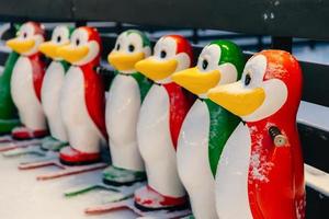 Horizontal shot of colorful skate aids in shape of funny penguins, needed to keep balance on ice rink, stand on ice covered with snow or skating arena photo