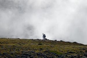 Tourists walking on the top of Serra da Estrela, the highest mountain of continental Portugal with thick clouds around. Travel and explore. People on the peak of the mountain. photo