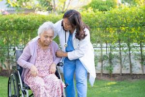 Doctor help and care Asian senior or elderly old lady woman patient sitting on wheelchair at park in nursing hospital ward, healthy strong medical concept. photo