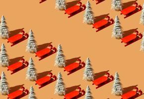 Pattern made with Christmas tree and red sleigh against pastel orange background. Christmas holiday idea. Minimal winter retro concept with copy space. photo