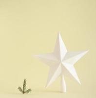 Big white star and small fir branch standing next to each other against yellow background. Minimal Christmas concept. with copy space. photo