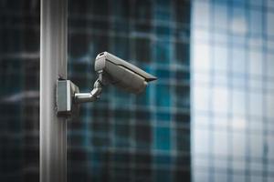 External security camera on pole in front of glass building wall photo