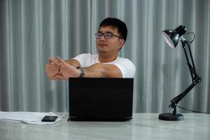 Asian man feels hurt his neck and shoulder during working on laptop computer for long time. Concept Office syndrome. Health problem. Self massage or streching to relief photo