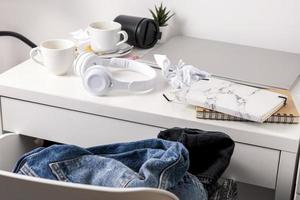 Messy table with laptop, dirty cups, and stationary items. Cluttered workplace, desk. Concept of being overwhelmed by working or studying. Mess and chaos at home. Deadline, stress. photo