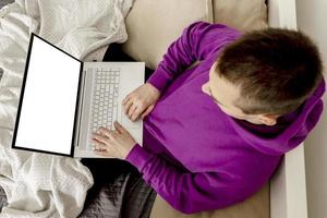 Man relaxing on bed and holding laptop computer. Mock up with blank white screen. Man using notebook to surf in internet, read news, watch movie, study or work online. App, game, web site presentation photo