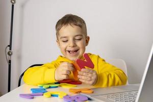 Adorable, cute, little boy learning alphabet online, with laptop at home. Child using e-learning platform to make a video call with his teacher and study. Homeschooling and distance education for kids photo