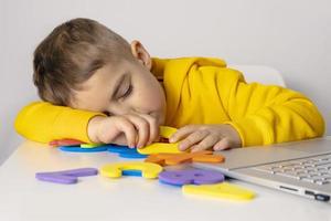 Little boy learning alphabet and numbers online, with laptop at home. Child is sad and tired. Negative emotions, stress, mental problems. Homeschooling and distance education for kids. photo