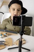 Adorable, cute, little boy blogger recording lifestyle blog, talking to camera of smartphone on tripod. Young influencer filming vlog for his channel. Child makes video for his followers online. photo
