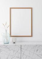 Empty vertical picture frame on white wall in modern living room. Mock up interior in minimalist, scandinavian style. Free space for picture. Marble console and dried grass in glass vase. 3D rendering photo