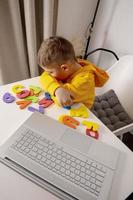 Little boy learning alphabet and numbers online, with laptop at home. Child is sad and tired. Negative emotions, stress, mental problems. Homeschooling and distance education for kids. photo