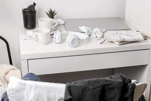 Messy table with laptop, dirty cups, and stationary items. Cluttered workplace, desk. Concept of being overwhelmed by working or studying. Mess and chaos at home. Deadline, stress. photo