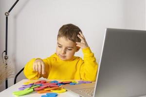 Adorable, cute, little boy learning alphabet online, with laptop at home. Child using e-learning platform to make a video call with his teacher and study. Homeschooling and distance education for kids photo