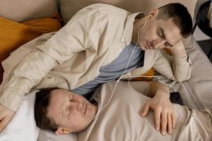 Happy gay couple with casual clothes spending time together at home and listening music with earphones. Two caucasian men relaxing. Homosexual relationships and alternative love. Cosy interior. photo