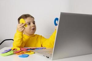 Adorable, cute, little boy learning alphabet online, with laptop at home. Child using e-learning platform to make a video call with his teacher and study. Homeschooling and distance education for kids photo