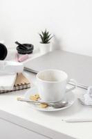 Messy table with laptop, dirty cups, and stationary items. Cluttered workplace, desk. Concept of being overwhelmed by working or studying. Mess and chaos at home. Deadline, stress. photo