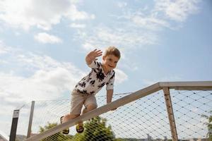 Adorable caucasian boy climbing on metal handrail outdoor. Cute child having fun in the city. Active leisure. Beautiful view, blue sky, amazing sunny weather. Go forward, climb to the top. photo