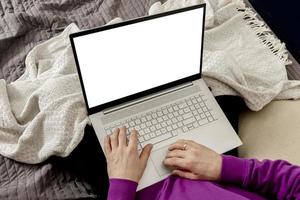 Man relaxing on bed and holding laptop computer. Mock up with blank white screen. Man using notebook to surf in internet, read news, watch movie, study or work online. App, game, web site presentation photo
