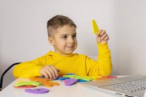 Adorable, cute, little boy learning alphabet online, with laptop at home. Child using e-learning platform to make a video call with his teacher and study. Homeschooling and distance education for kids photo