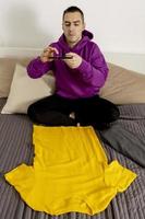 Man with violet hoodie using digital tablet, takes a photo of his old clothes to sell them online. Selling on website, e-commerce. Reuse, second-hand concept. Conscious consumer, sustainable lifestyle