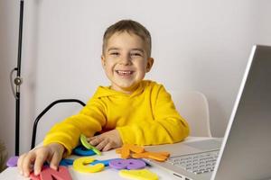 Adorable, cute, little boy learning alphabet online, with laptop at home. Child using e-learning platform to make a video call with his teacher and study. Homeschooling and distance education for kids photo