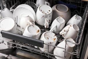 Unwashed, dirty dishes in dishwasher. Mess in the kitchen. Dirty kitchenware, plates and mugs. Messy dishware. Close up view. photo