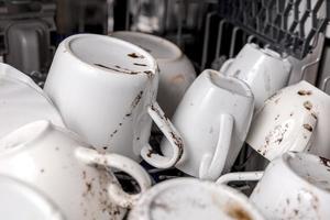 Unwashed, dirty dishes in dishwasher. Mess in the kitchen. Dirty kitchenware, plates and mugs. Messy dishware. Close up view. photo