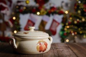 olla de cerámica sobre mesa de madera. fondo con adornos navideños.