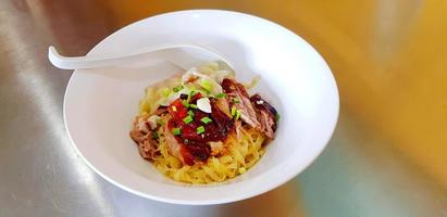 Dry grilled duck noodles and dumpling or dough with topping spring onion sliced and spoon on white bowl. Asian food in Hong Kong or Chinese style on stainless steel table at restaurant. photo