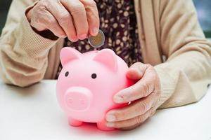 Retired elderly woman putting coins money in piggy bank and worry about monthly expenses and treatment fee payment. photo