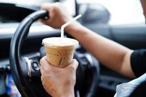 Bangkok, Thailand - May 15, 2022 Asian woman driver hold ice coffee cup for drink in car, dangerous and risk an accident. photo