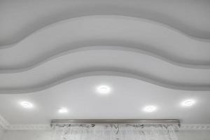 suspended ceiling with halogen spots lamps and drywall construction  with intricate crown molding in empty room in apartment or house. Stretch ceiling white and complex shape. photo