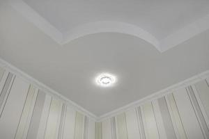 suspended ceiling with halogen spots lamps and drywall construction  with intricate crown molding in empty room in apartment or house. Stretch ceiling white and complex shape. photo